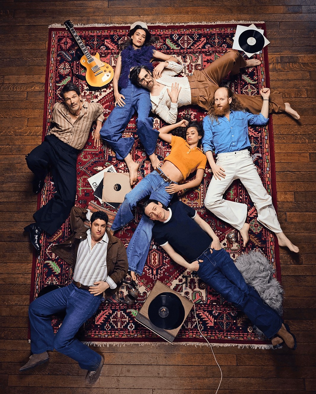 Band members lying on a rug, surrounded by musical instruments and records.