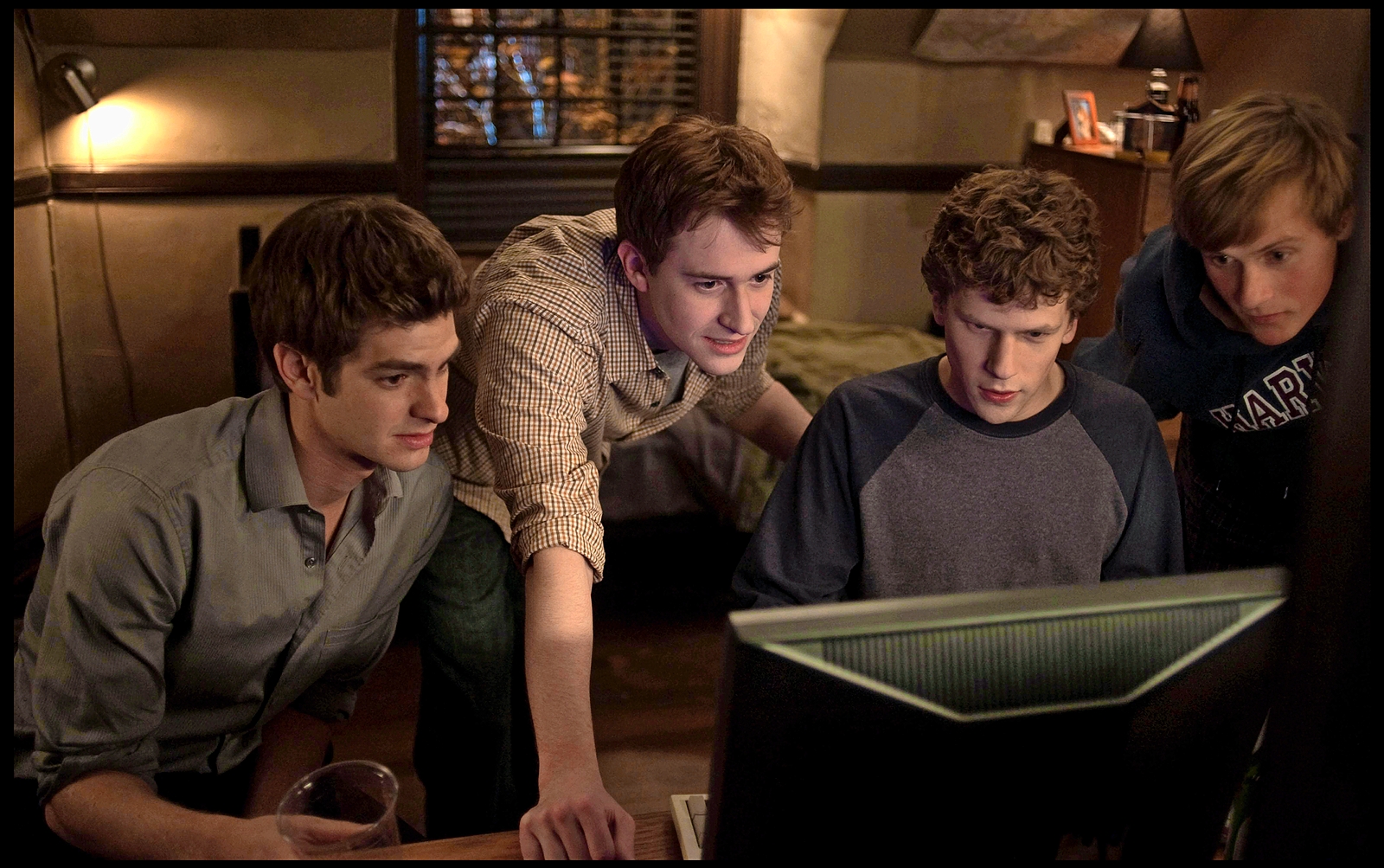 Scene from The Social Network showing four young men looking at a computer screen.