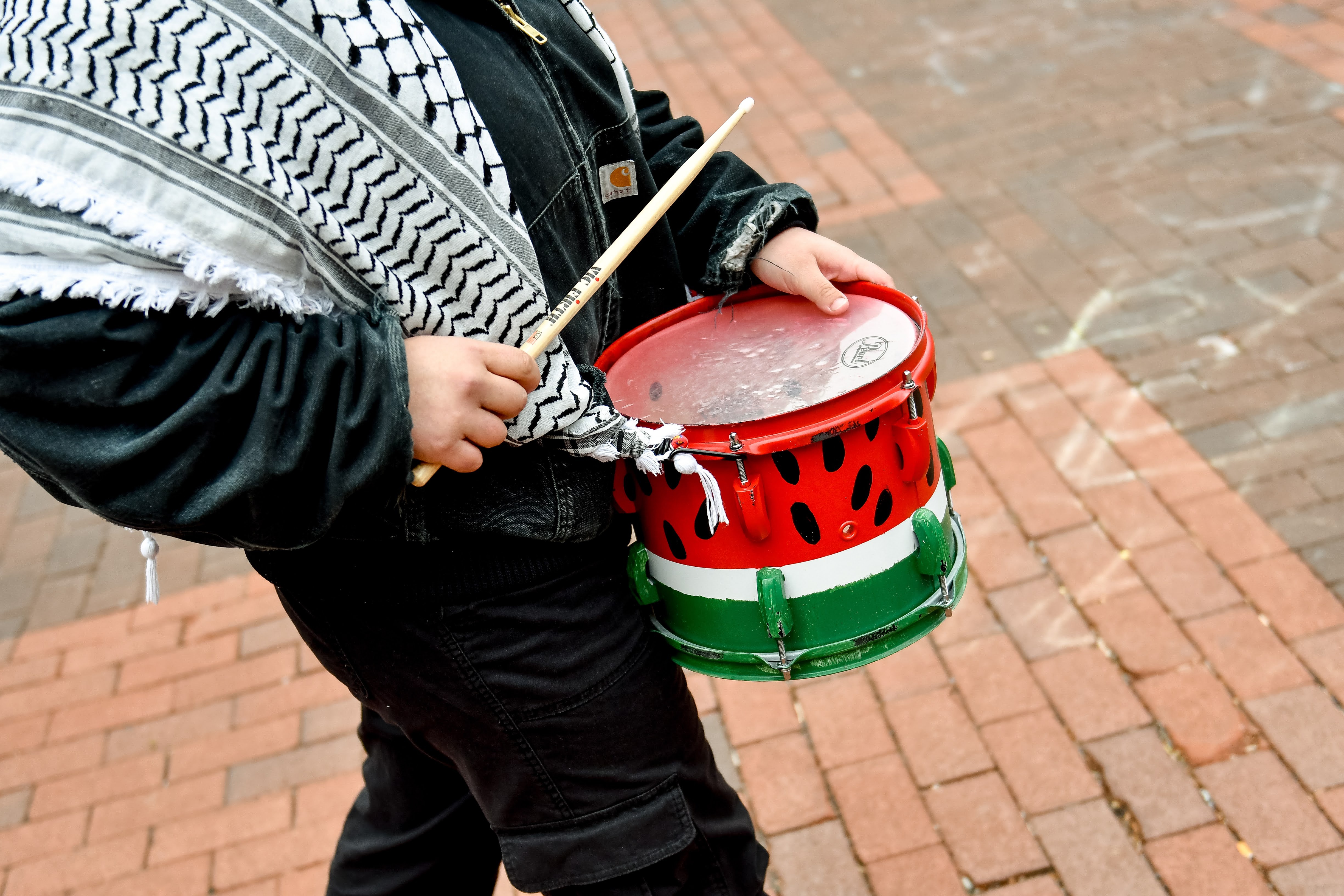 Person playing a watermelon-painted drum at a protest.