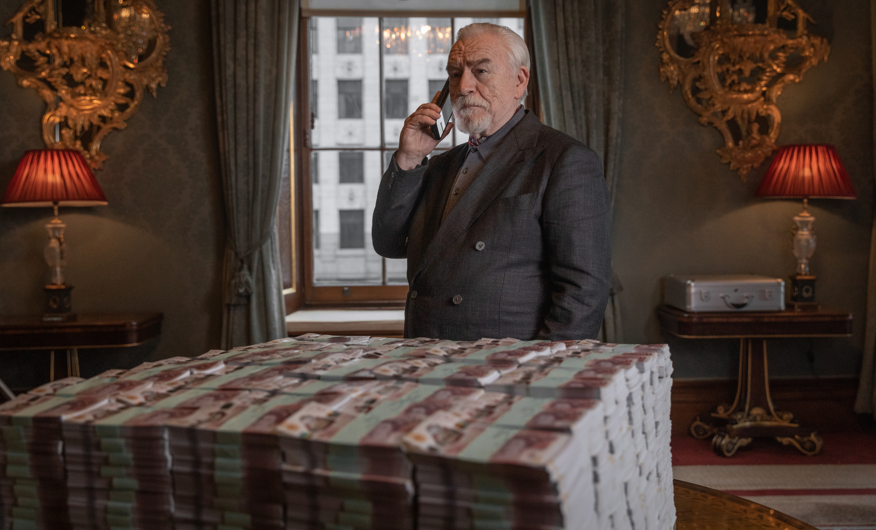 a man in a suit talks on a cell phone in front of a stack of money