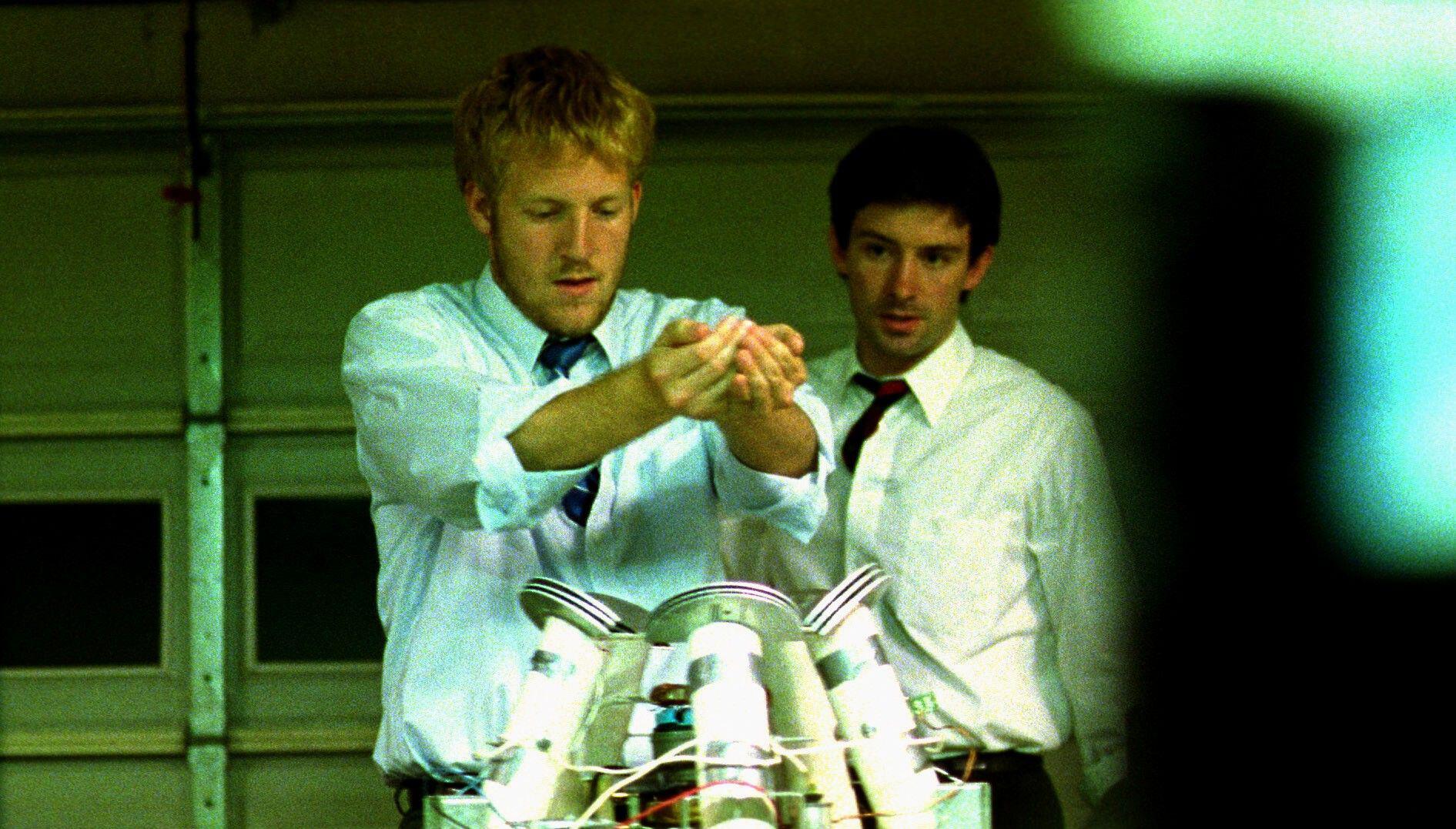 Two men in suits work on a time travel device.